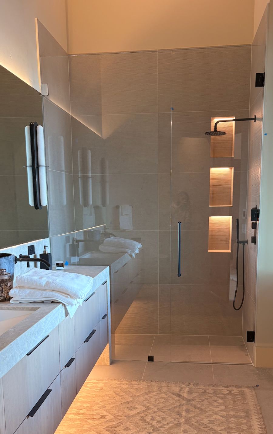 Finished curbless primary shower with lit triple niche and floating vanity