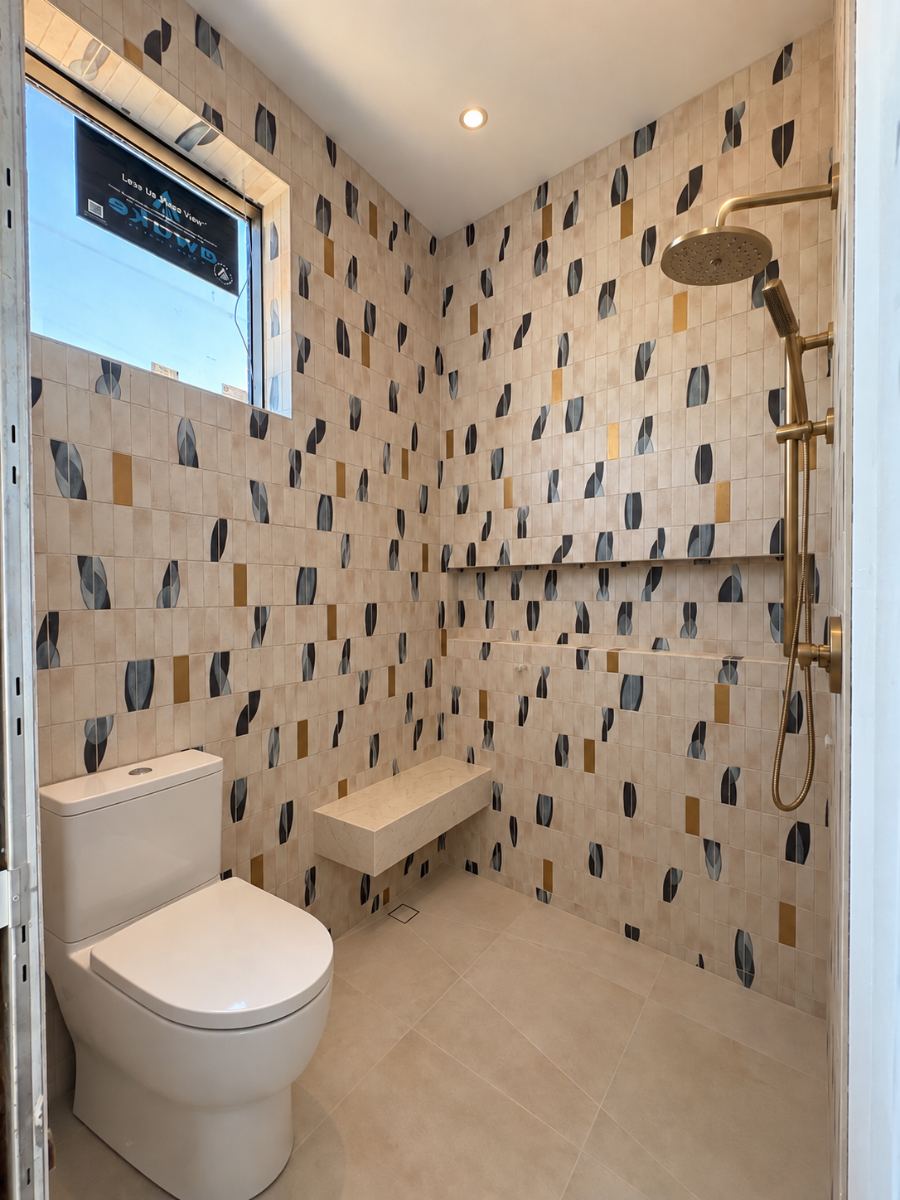 Finished curbless shower with patterned mosaic tile, floating bench and brass fixtures